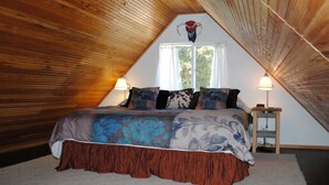 Une chambre avec un plafond en pente, un lit recouvert d’une couvre-lit à motifs floraux, deux lampes de chevet et une fenêtre avec des rideaux.