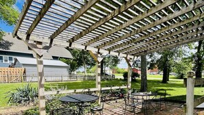 A covered patio area with brick flooring, metal tables, and chairs.