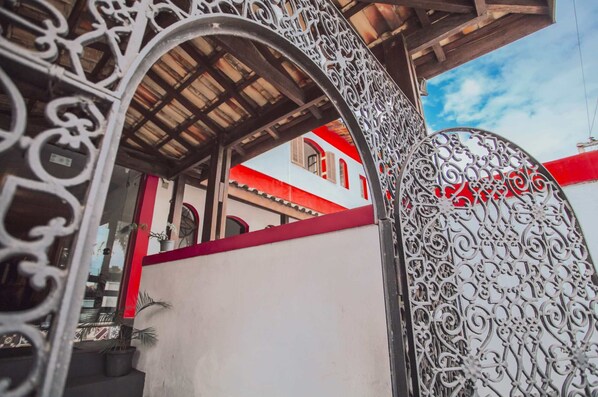 Una ornamentada verja metálica con diseños intrincados, que da acceso a un edificio con fachada roja y blanca.