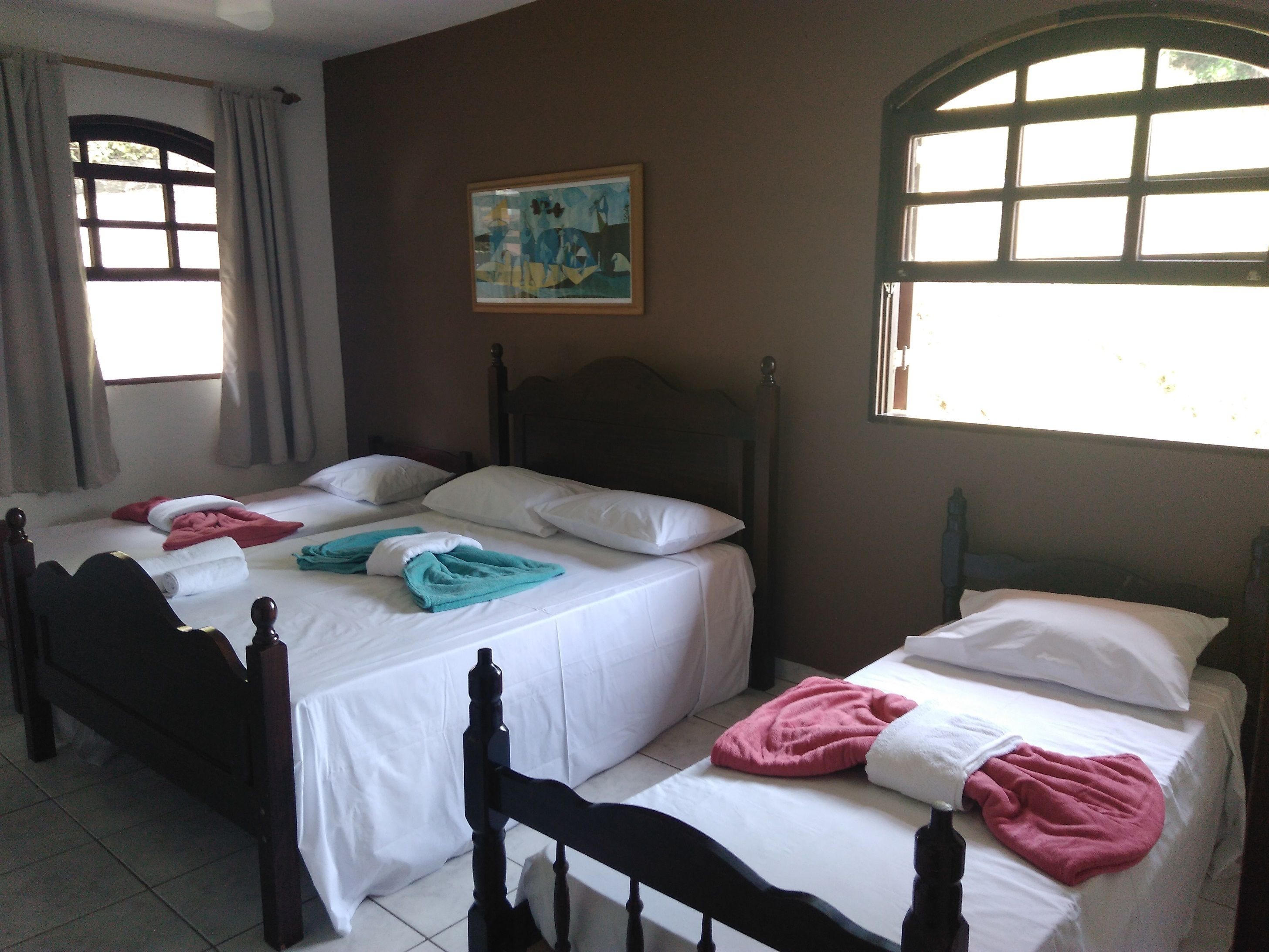 Ein Hotelzimmer mit zwei Betten, einem Bild an der Wand und großen Fenstern.
