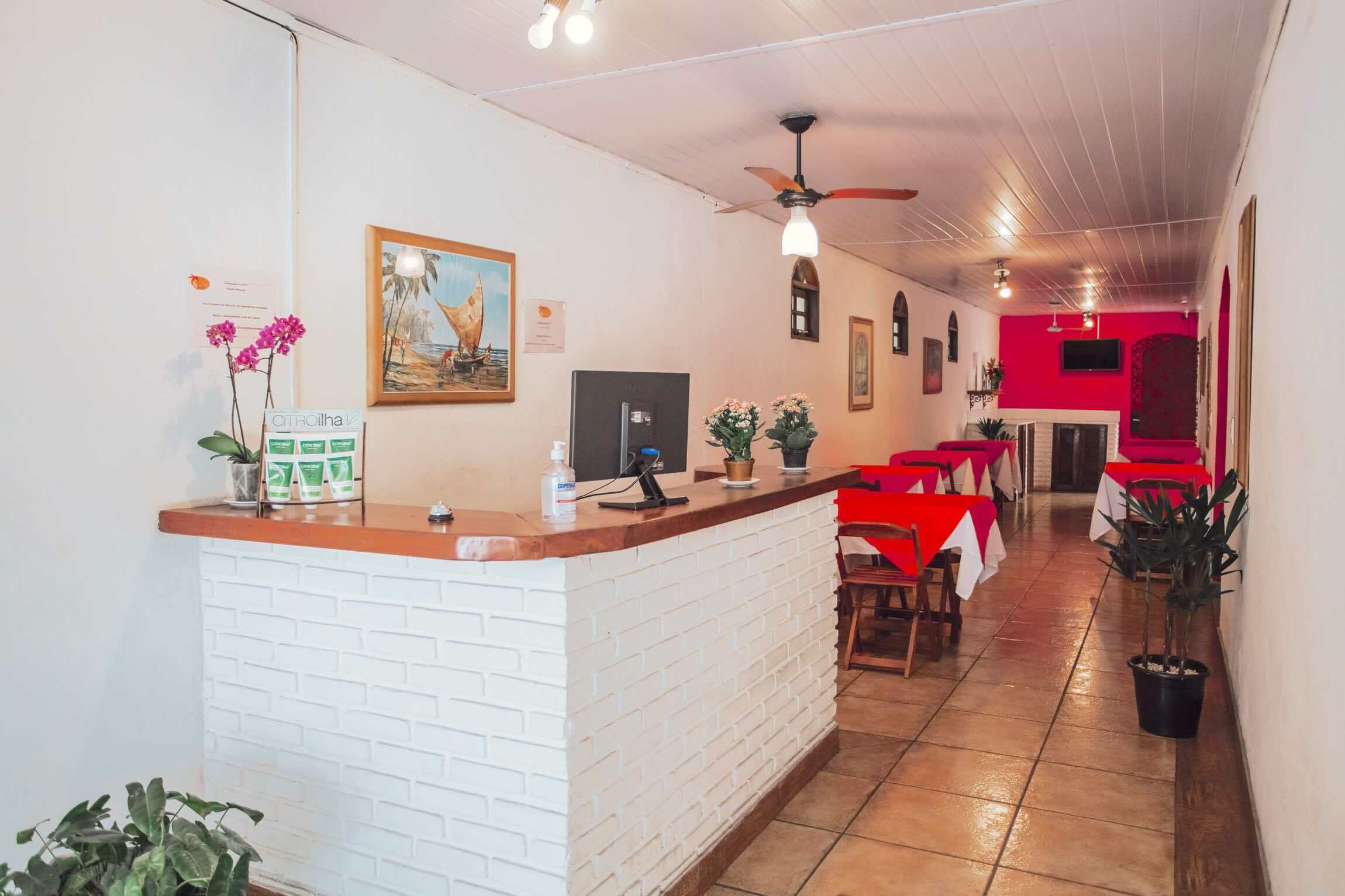 Un espace d’accueil d’hôtel avec un comptoir en briques blanches, un ventilateur de plafond et des tables rouges et blanches.