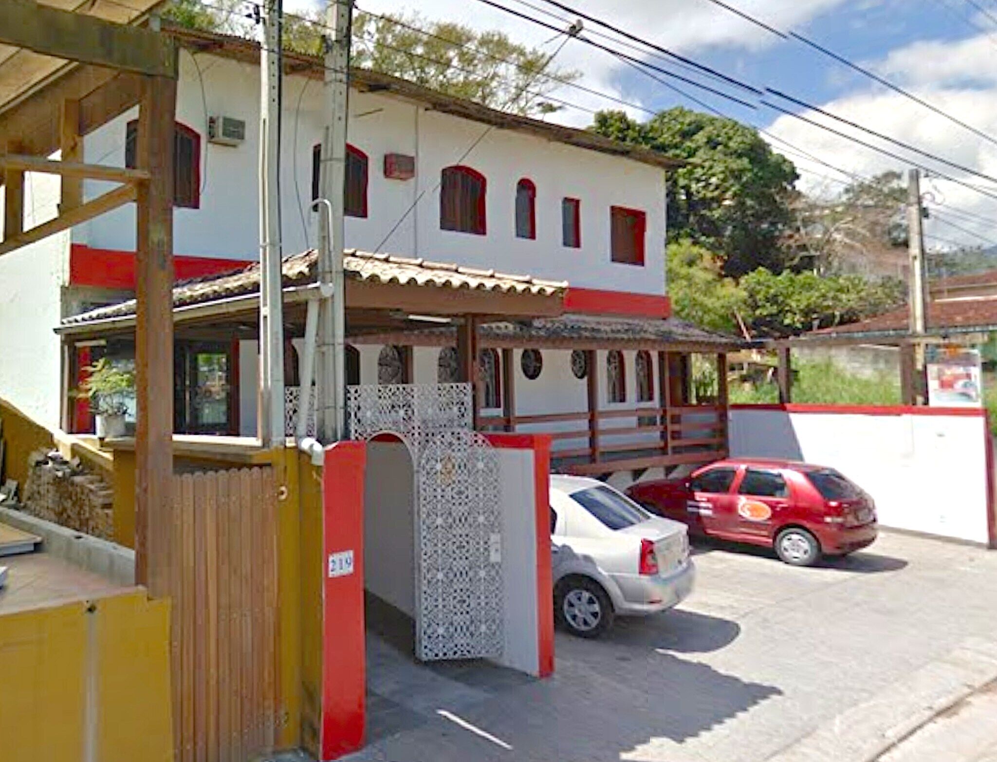 Un edificio de dos pisos con fachada roja y blanca, un porche cubierto y una entrada protegida por una reja.