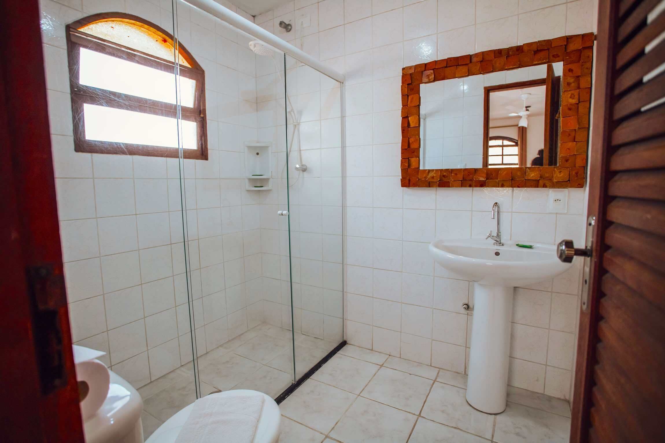 A bathroom with a glass shower enclosure, a white sink, and a mirror with a wooden frame.