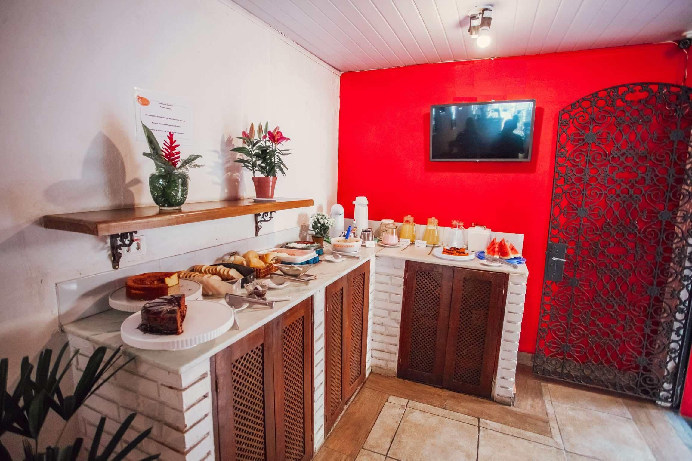 A kitchen with a red accent wall, a mounted TV, and various food items on the counter.