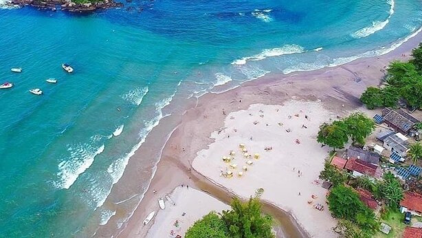 Ein Luftbild eines Strandes mit klarem, blauem Wasser, einem sandigen Ufer und einer kleinen Insel mit Felsen.