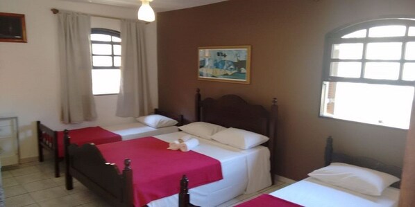 A room with two single beds, a wooden headboard, a small table, and a window with curtains. - Pousada Chalé Suisso (Ilhabela)
