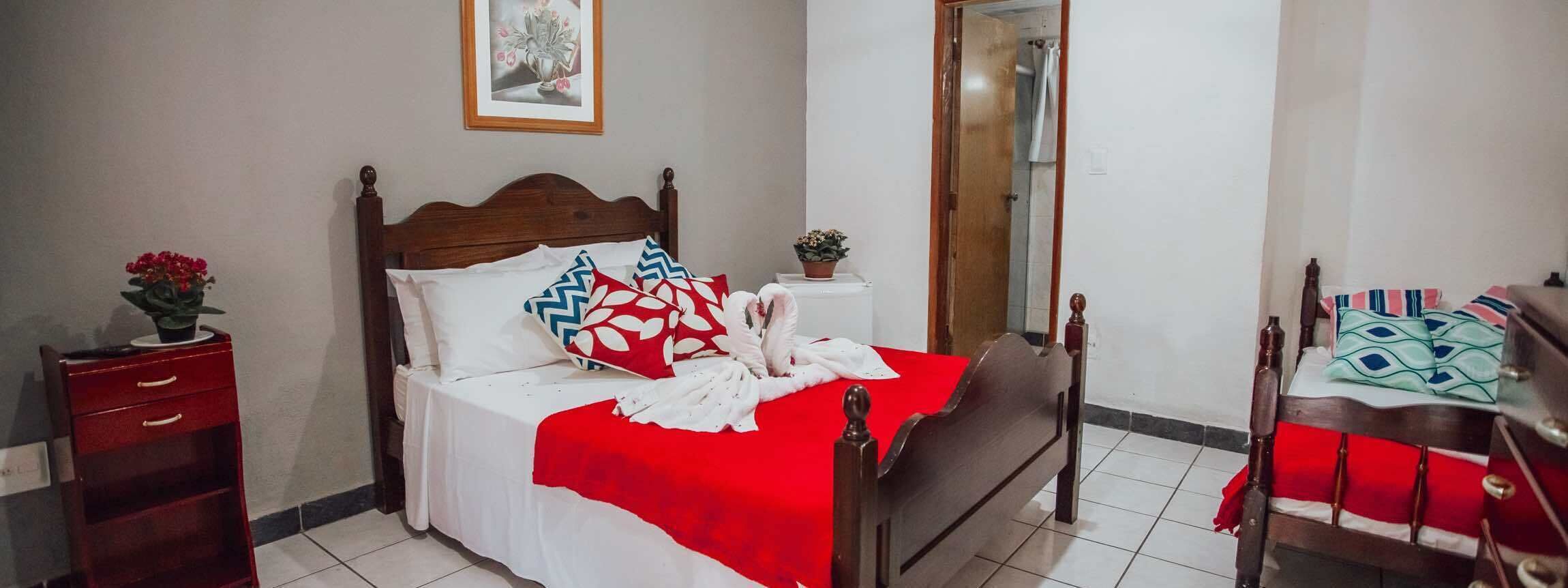 Une chambre à coucher bien rangée, avec un lit en bois, une couvre-lit rouge et blanche, et une petite table de chevet agrémentée d’une plante.