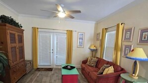 A living room with a red sofa, a small table, a ceiling fan, and wooden flooring. - Key West - Stock Island  (Key West)