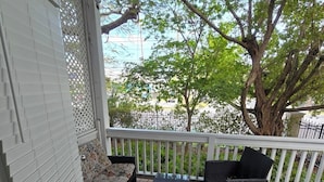 A covered porch with wooden flooring, a sofa, two black wicker chairs, and a glass-top coffee table. - Key West - Stock Island  (Key West)