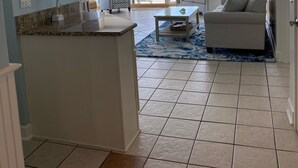 A spacious living area with a large window overlooking the ocean, a ceiling fan, and a central island with a marble countertop. - One Ocean Place 1101! 
Book at 2024 Rates w/ VRBO all in pricing nightly rate! (Murrells Inlet)