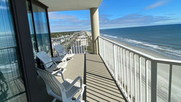 A balcony with white chairs and a view of the beach. - One Ocean Place 1101! 
Book at 2024 Rates w/ VRBO all in pricing nightly rate! (Murrells Inlet)