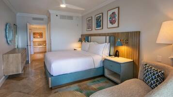 Habitación de hotel con cama, mesitas de noche, sofá, ventilador de techo y obras de arte en las paredes.