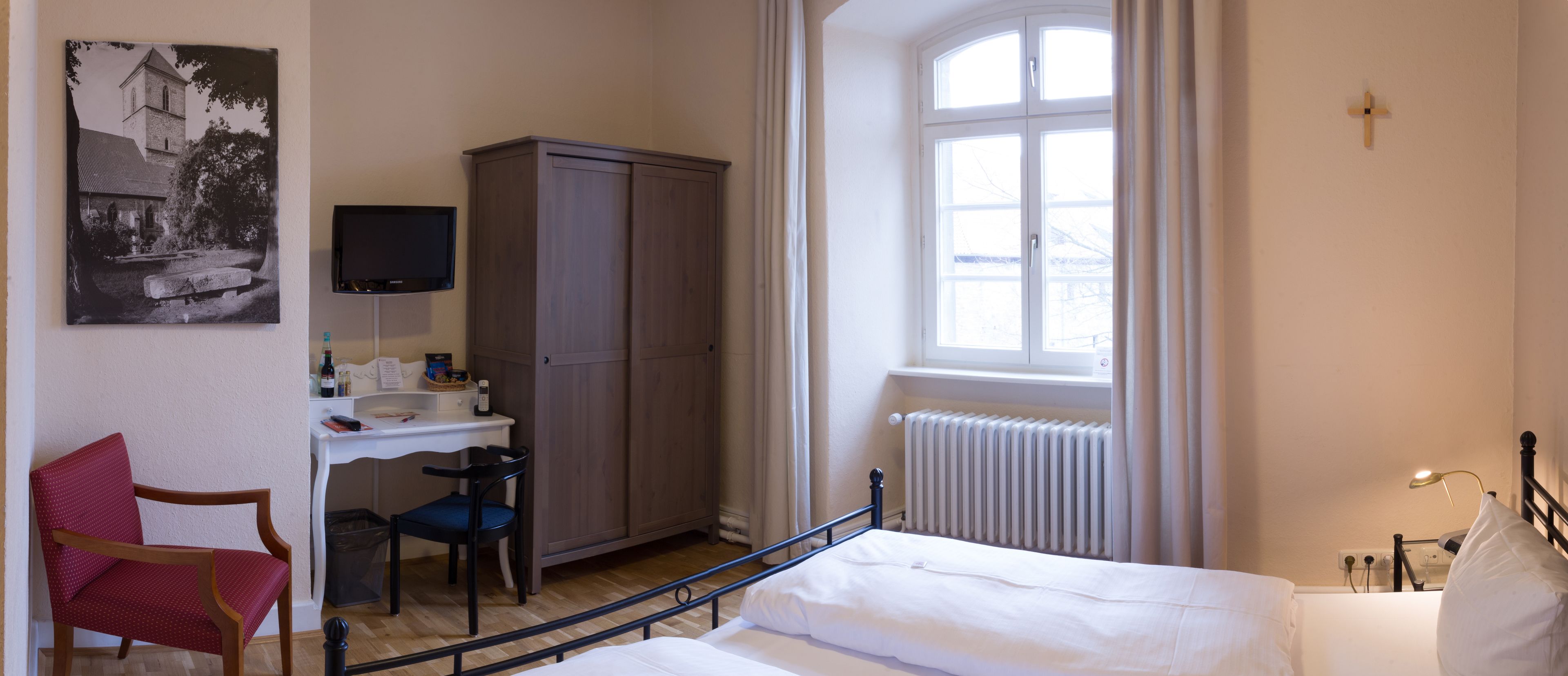 Ein Schlafzimmer mit Bett, Schreibtisch, Stuhl, Kleiderschrank, Fenster und Fernseher.