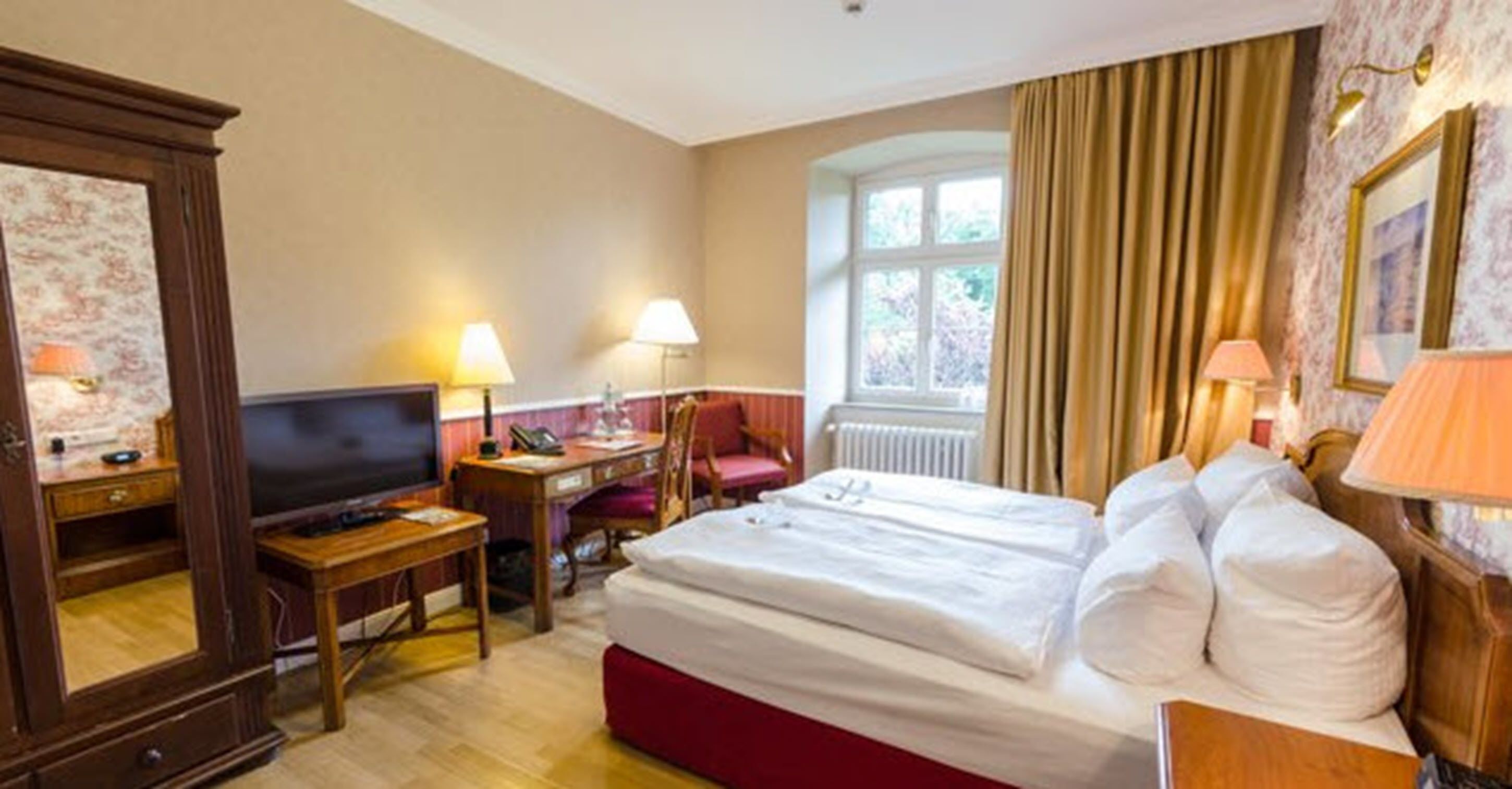 Habitación de hotel con cama, escritorio, silla, televisión y ventana con cortinas.