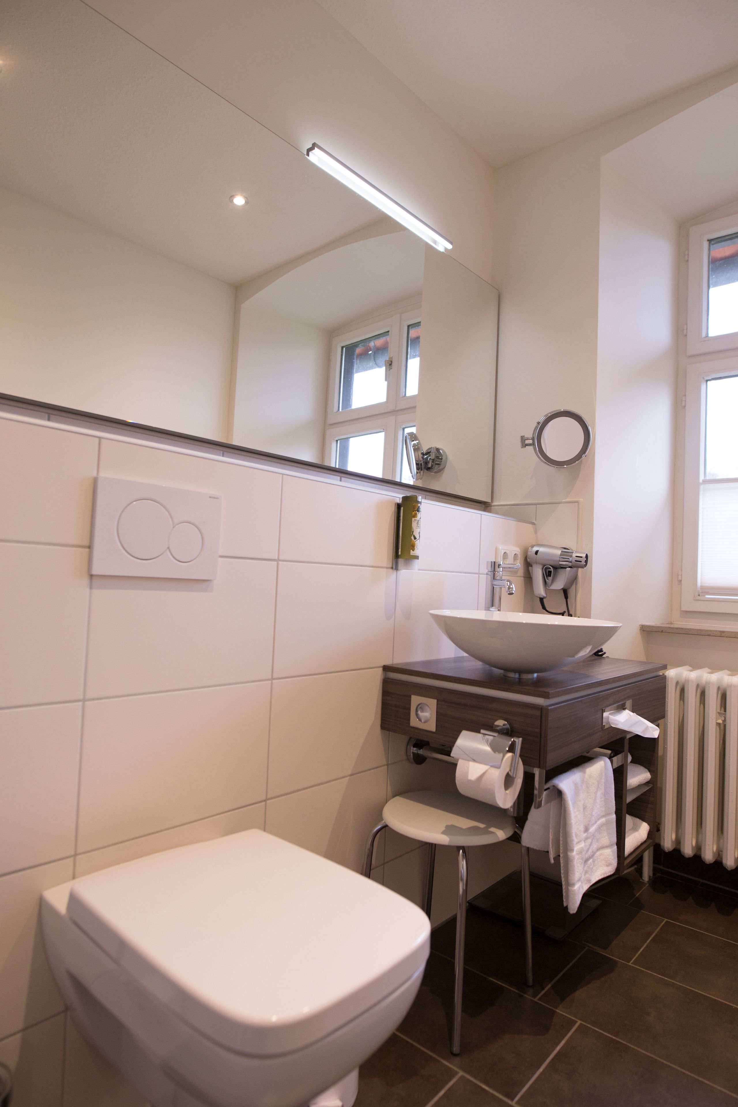 A modern bathroom with a white toilet, a vessel sink, a mirror, and a towel rack.