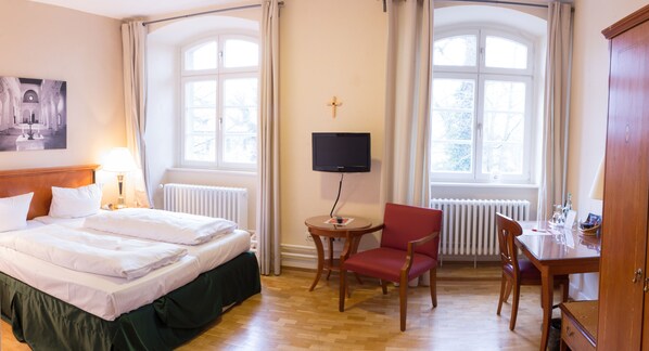 A hotel room with a bed, a TV, a chair, a desk, and a window with curtains. - Klosterhotel Wöltingerode (Goslar)