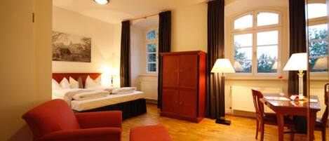 A hotel room with a bed, a desk, a chair, a wardrobe, and a window with curtains.