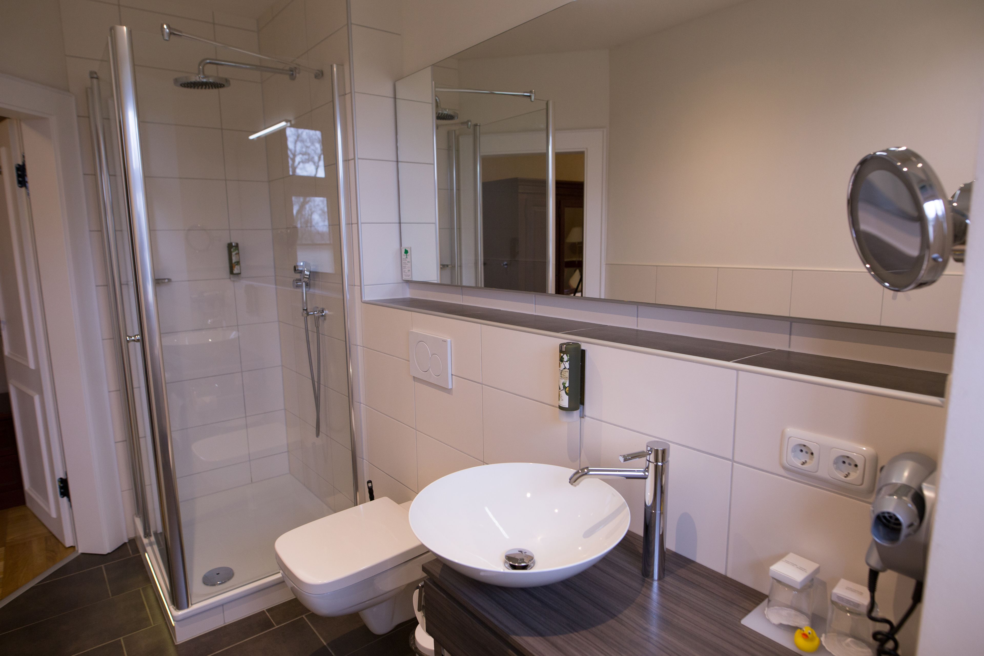 Un baño moderno con cabina de ducha de vidrio, un lavamanos blanco y un espejo grande.