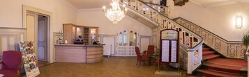 Eine großzügige Lobby mit einer Treppe, einem Empfangsbereich und einem Schild, das den Weg zum Restaurant und Speisesaal weist.
