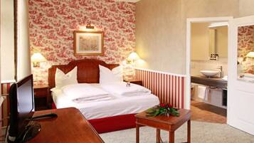 A hotel room with a bed, bedside table, lamp, and a small table with a flower arrangement.
