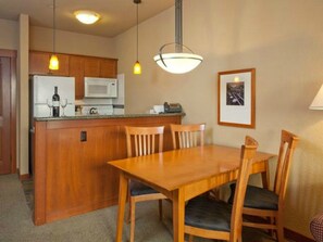 Una cocina compacta con armarios de madera, un microondas y una zona de comedor con una mesa y sillas de madera.
