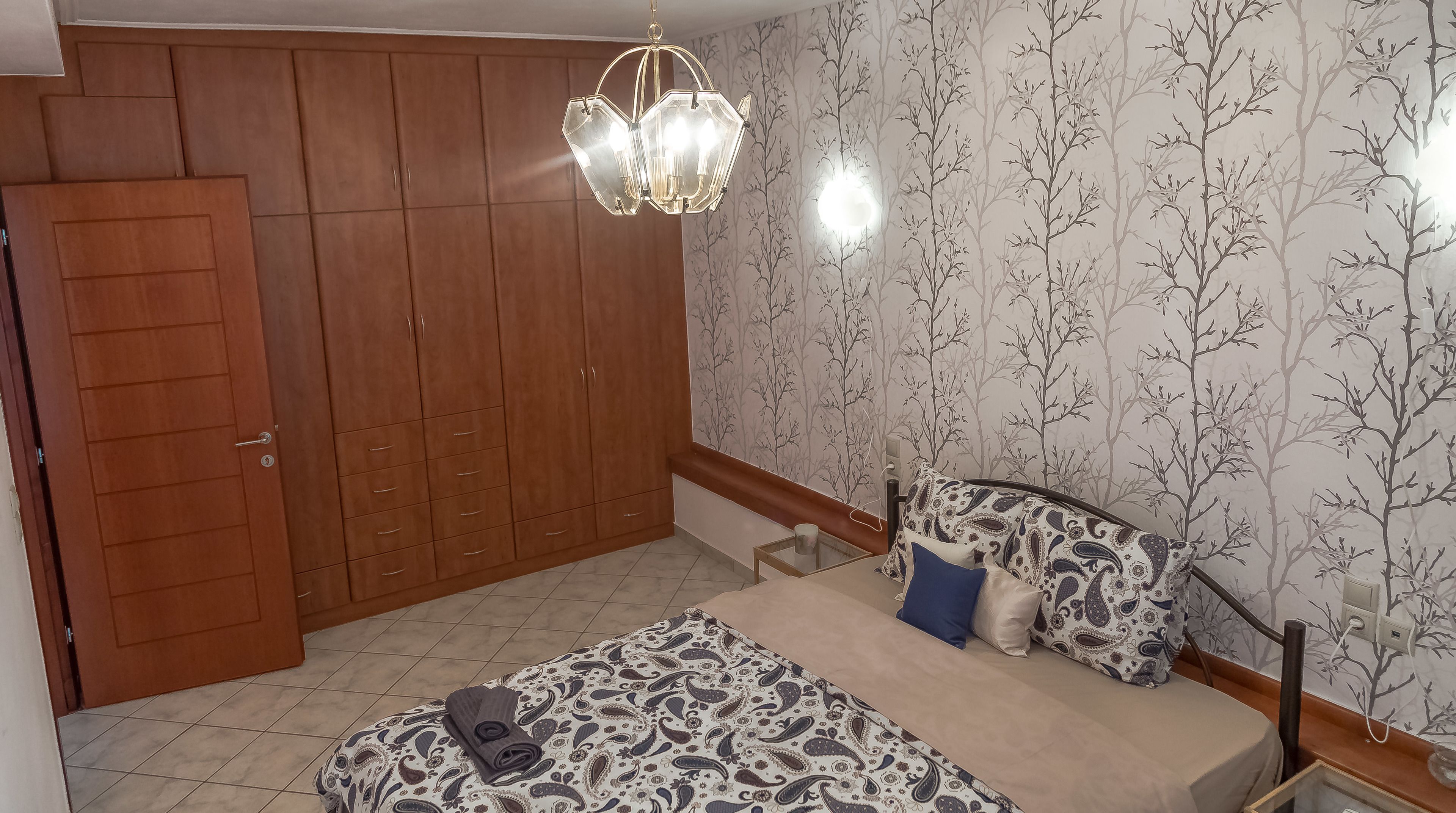 Une chambre à coucher avec un lit, une armoire, un lustre et un papier peint à motifs.