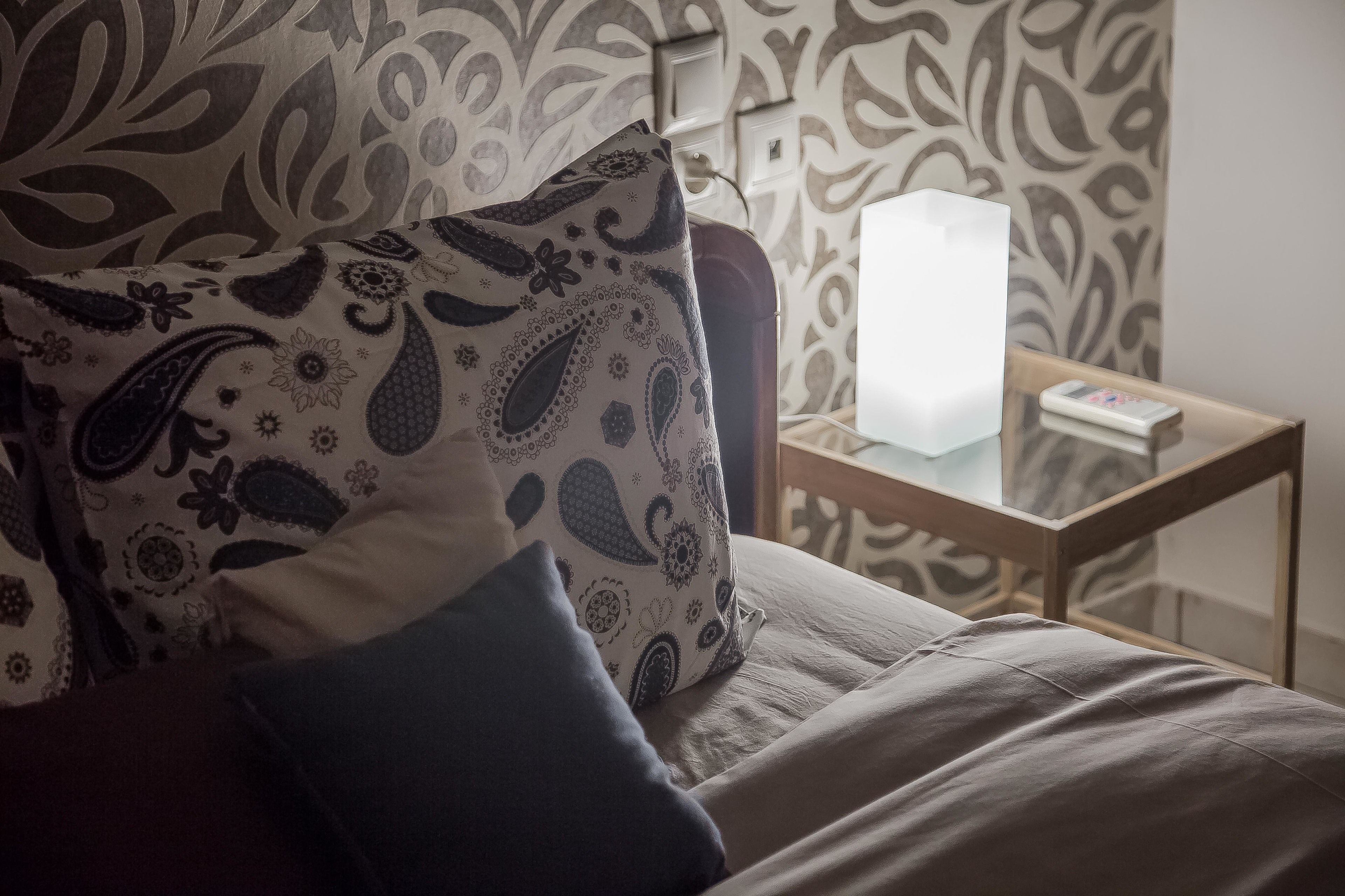 A bed with patterned pillows, a bedside table with a lamp, and a patterned wall.