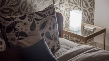 A bed with patterned pillows, a bedside table with a lamp, and a patterned wall.