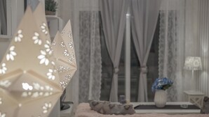 Un salon chaleureux avec un canapé moelleux, un arbre décoratif en papier et un vase rempli de fleurs bleues posé sur un rebord de fenêtre.