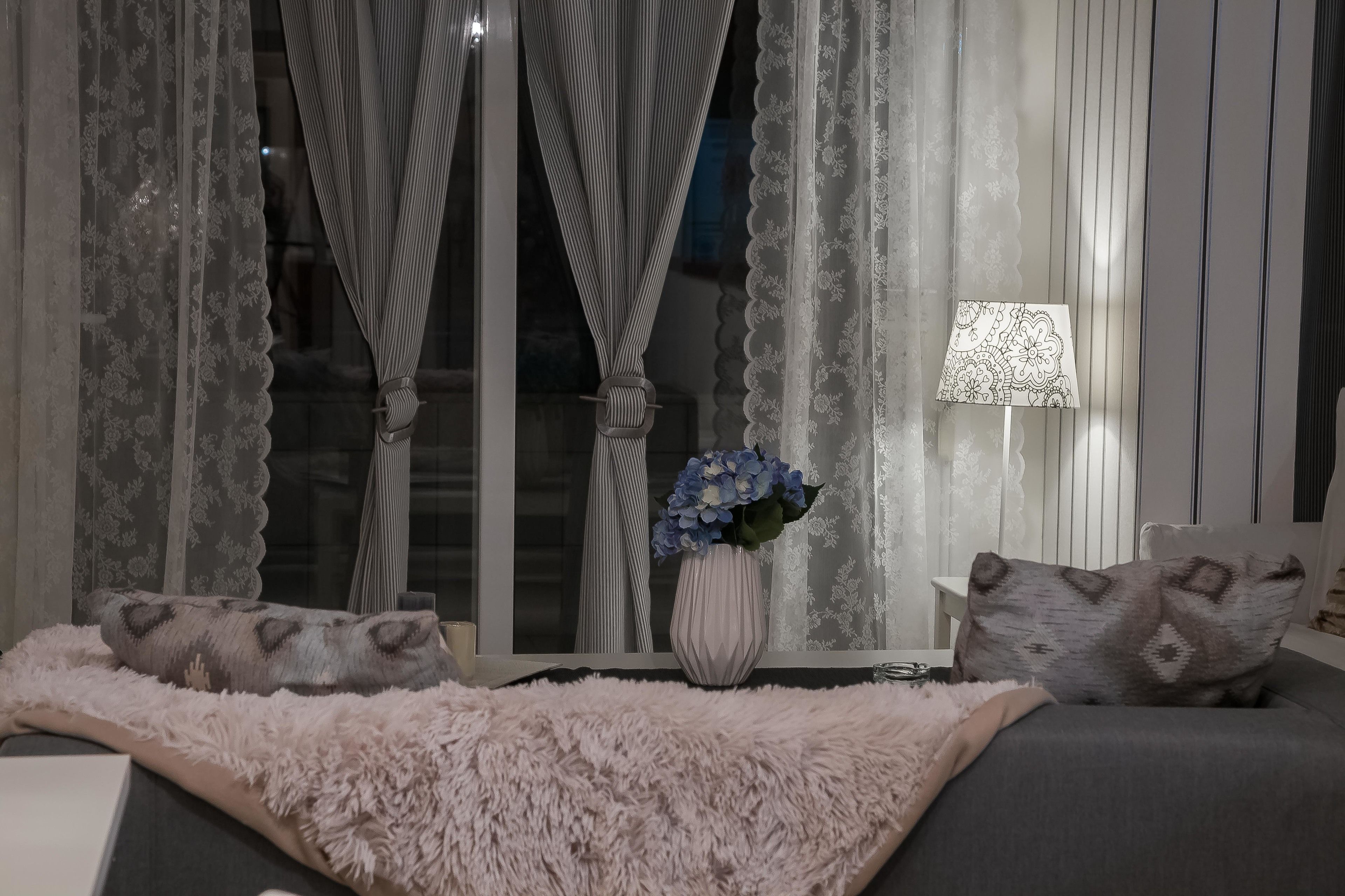 Une pièce chaleureuse avec un lit, un plaid rose moelleux, un vase rempli de fleurs et une lampe.