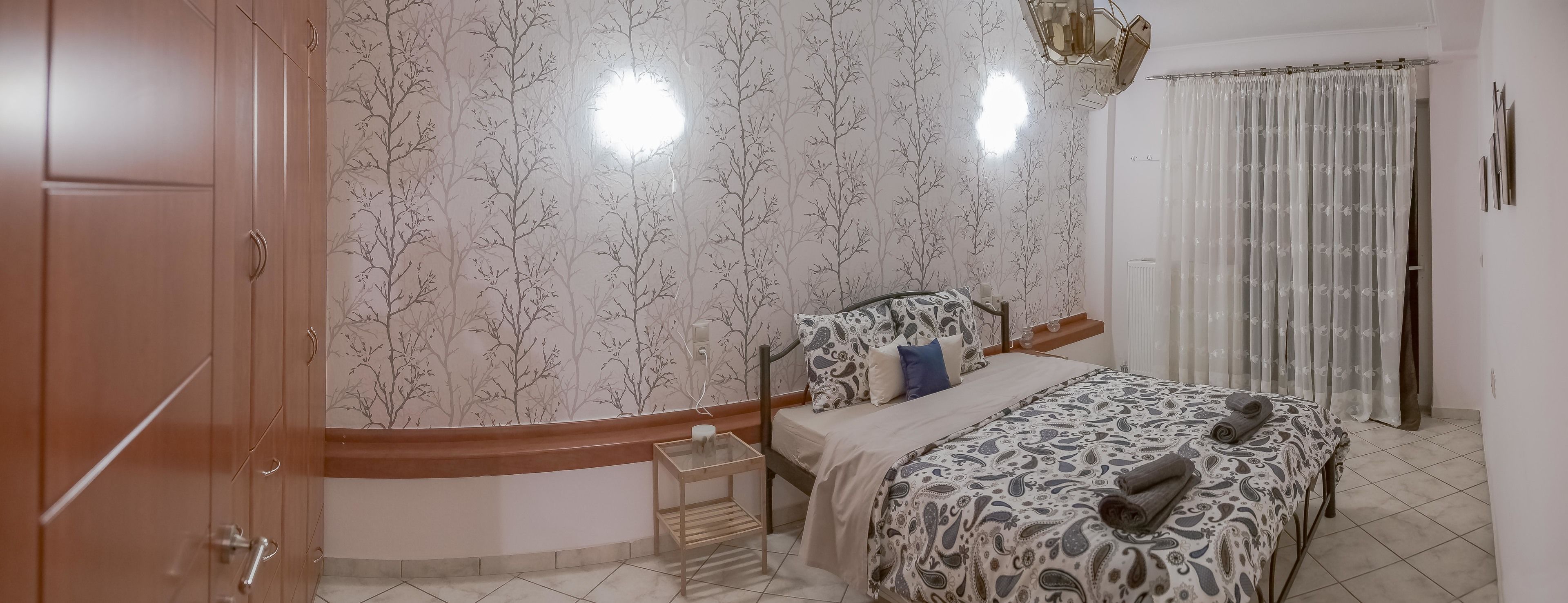 A bedroom with a bed, a nightstand, a wardrobe, and a window with curtains.