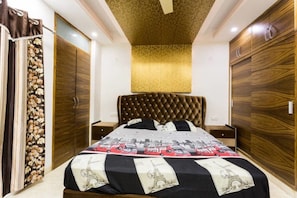 Une chambre à coucher avec une tête de lit capitonnée, un lit recouvert d’une couvre-lit à motifs, des armoires en bois et un plafond décoratif.