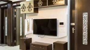 A modern living room with a flat-screen TV mounted on the wall, dark wooden cabinets, and decorative wall panels.
