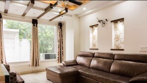A living room with a sectional sofa, a small ottoman, a television, and a window with curtains.