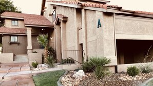 Un edificio residencial con garaje, césped bien cuidado y un pequeño jardín con diversas plantas.