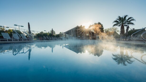 Una piscina cristalina con sillas de descanso y un edificio al fondo.