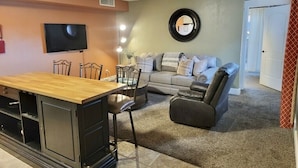 Una sala de estar con una mesa de comedor de madera, un sofá, un sillón reclinable, un televisor y un espejo fijado a la pared.