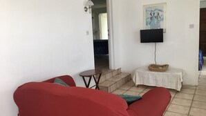 Een woonkamer met een rode bank, een klein tafeltje met een mand, en een aan de muur bevestigde televisie.