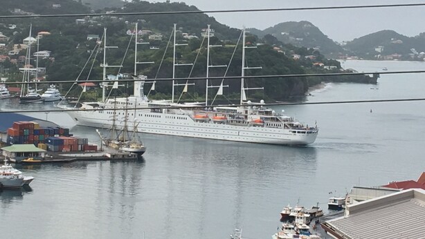 Een groot cruiseschip ligt aangemeerd in een haven, met uitzicht op de omliggende heuvels en gebouwen.