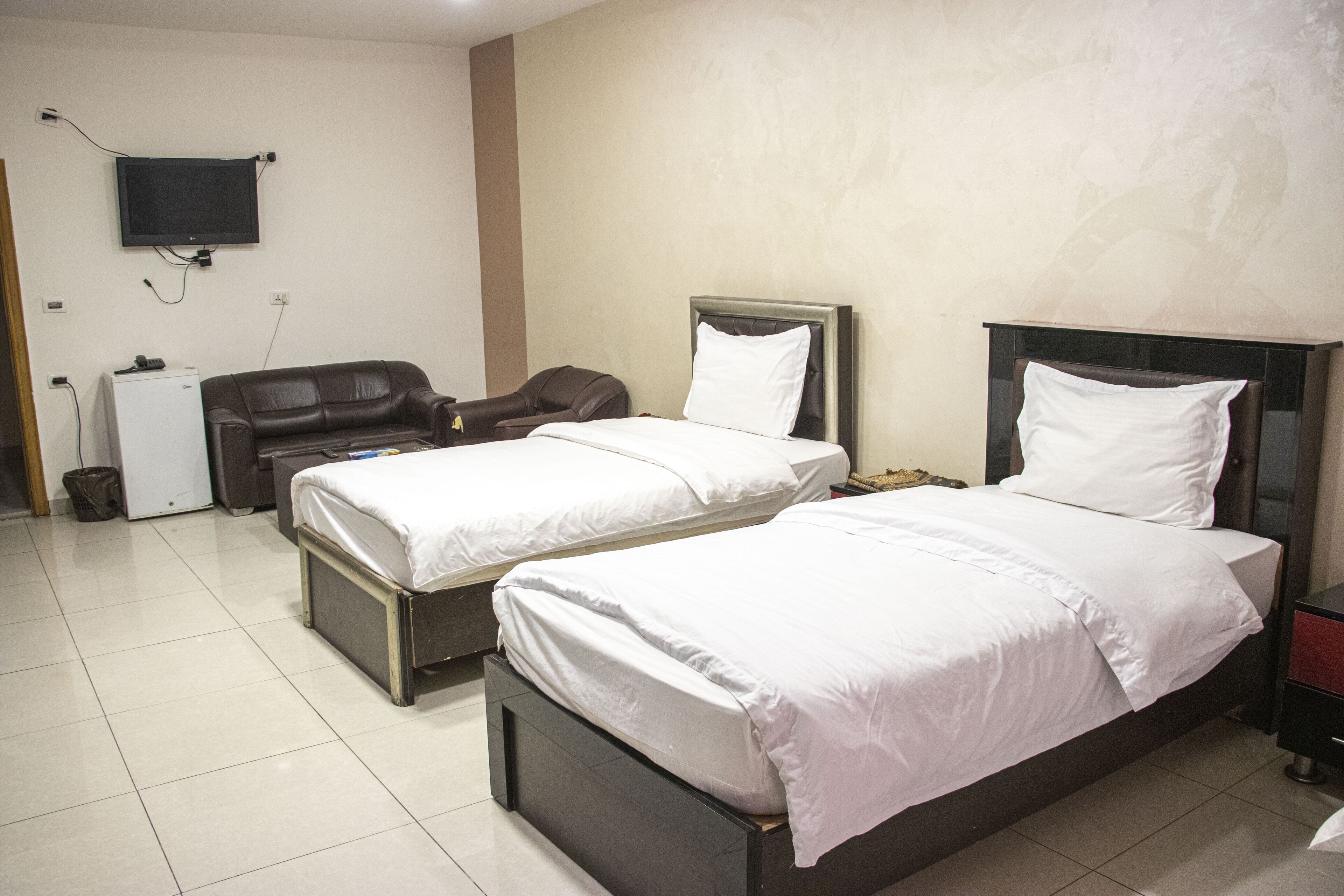 A hotel room with two single beds, a desk with a chair, a television mounted on the wall, and a trash bin.