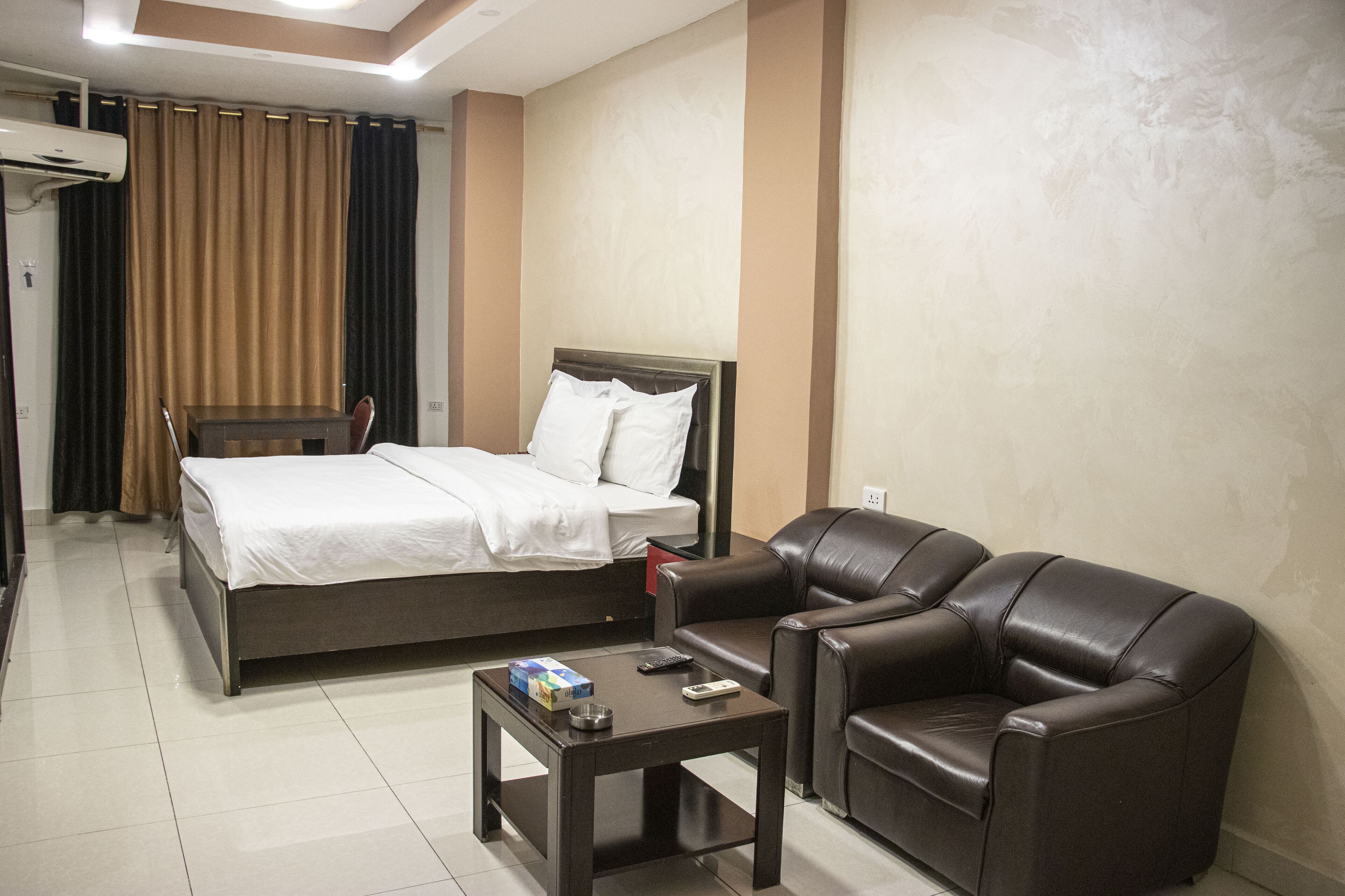 A hotel room with a bed, a leather sofa, a small table, and a TV.