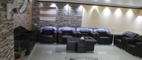 A living room with a sectional sofa, a coffee table, and a fan. There is a stone wall and a window with blinds.