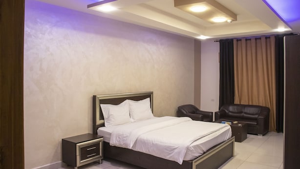 A modern bedroom with a bed, nightstands, a seating area with a sofa and armchair, and a ceiling with recessed lighting. - Sara Crown Hotel (Irbid)