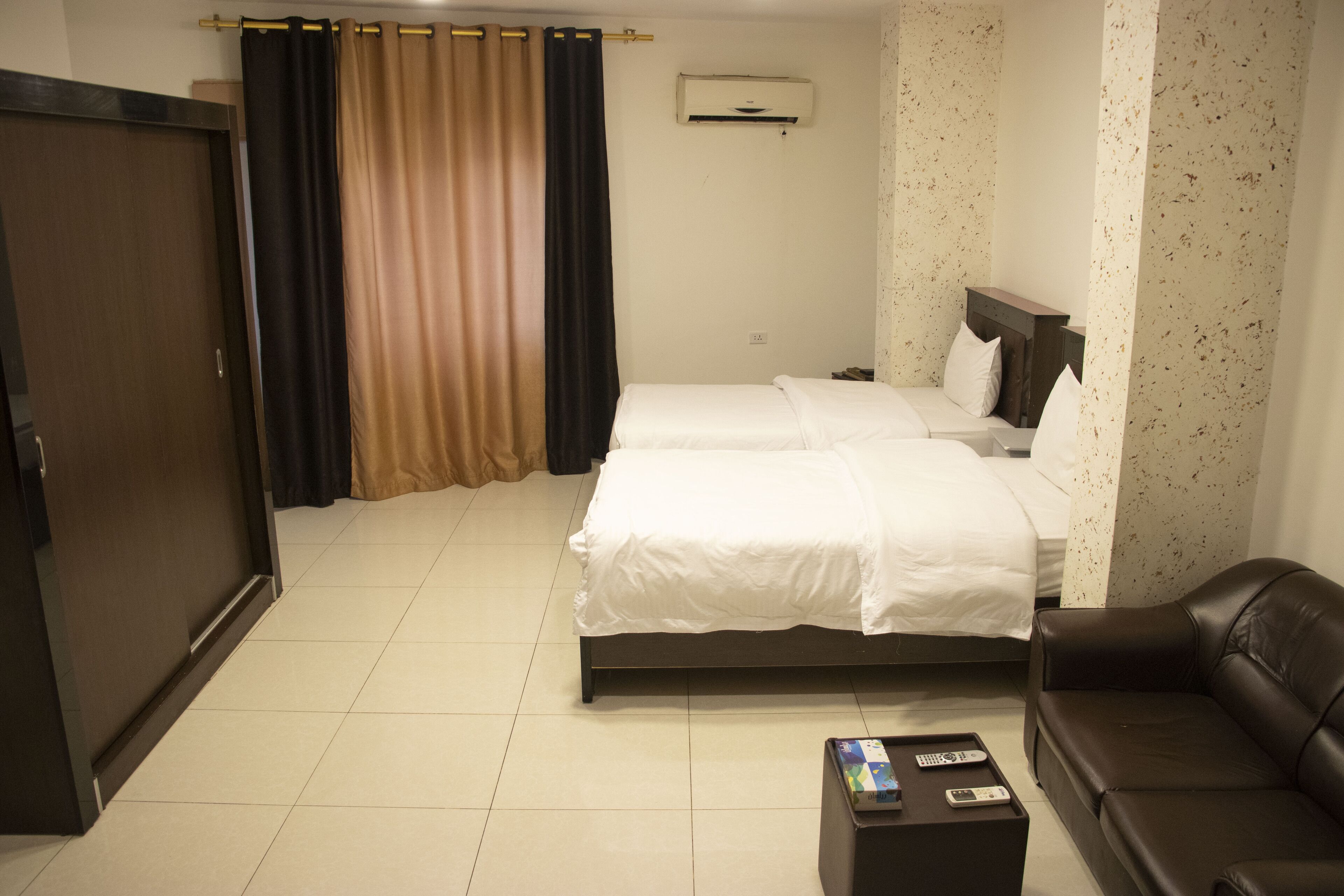 A hotel room with two beds, a sofa, a coffee table, and an air conditioning unit.