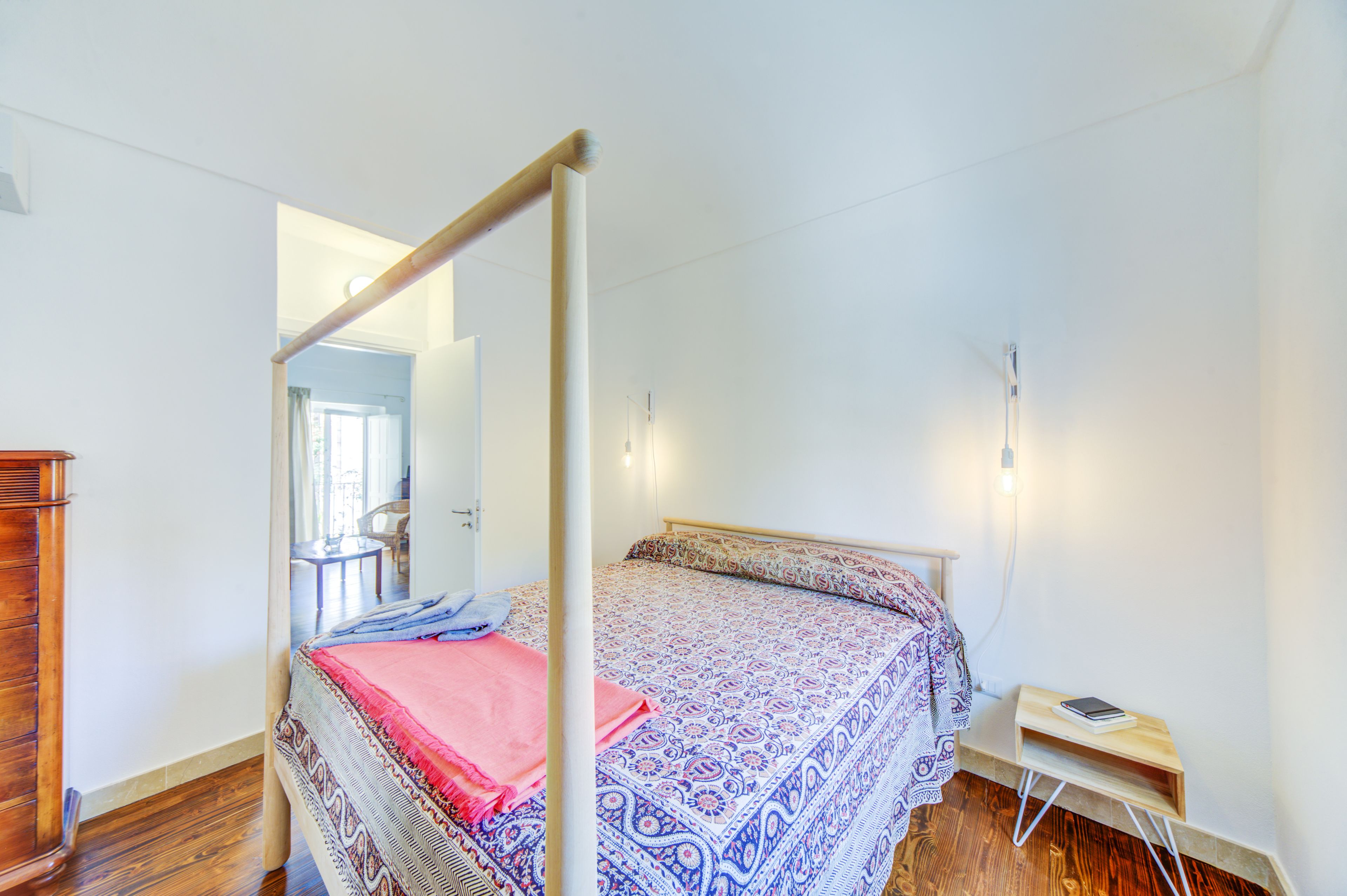 Ein Schlafzimmer mit einem Himmelbett, einem hölzernen Schminktisch und einem kleinen Nachttisch mit Lampe.