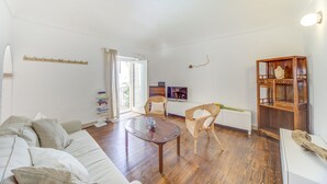 Ein geräumiges Wohnzimmer mit Holzboden, einer Couch, zwei Korbstühlen, einem Couchtisch und einer Holzkommode mit Dekorationen.