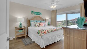 Una camera da letto con un letto, un comodino, una ventola a soffitto, una finestra con vista e la parola 'Beach' sulla parete.