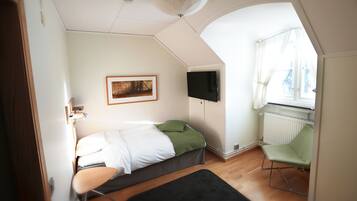 A bedroom with a bed, a green chair, a framed picture on the wall, and a window with curtains.