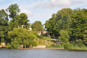A lakeside view with a dock, trees, and a building in the background.