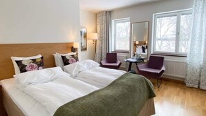 Ein Hotelzimmer mit einem großen Bett, zwei Sesseln, einem kleinen Tisch und einem Fenster mit Vorhängen.